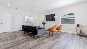 A modern living room with a grey sofa, orange chairs, and a flat-screen TV mounted on the wall. - Miami Dual Oasis Retreat | Fast WiFi & Parking (Miami)