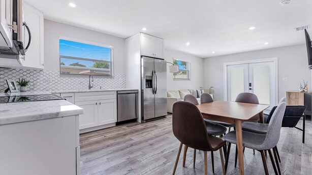 A modern kitchen with white cabinets, stainless steel appliances, and a dining area with a wooden table and chairs. - Miami Dual Oasis Retreat | Fast WiFi & Parking (Miami)