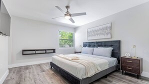 A bedroom with a bed, a nightstand, a ceiling fan, a window, and a wall-mounted shelf. - Miami Dual Oasis Retreat | Fast WiFi & Parking (Miami)