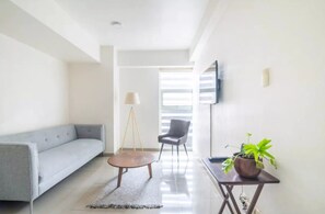 Una sala de estar moderna con un sofá gris, una mesa de centro redonda, una lámpara de pie, una silla y una planta en maceta.