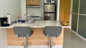 A modern kitchen with two bar stools, a microwave, and a refrigerator.