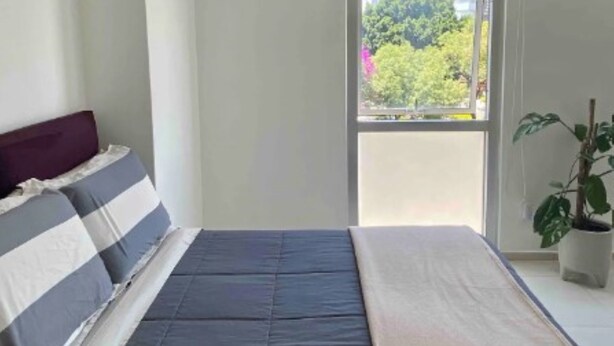A bedroom with a bed, a window, and a potted plant.