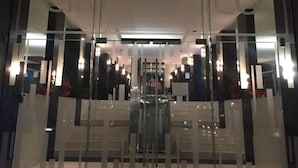 A modern hotel lobby with a central elevator, glass partitions, and a symmetrical design.