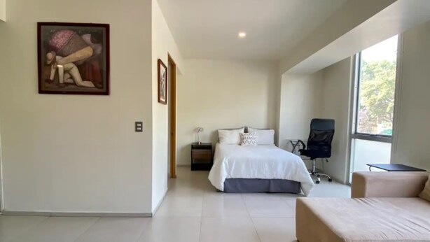 A modern bedroom with a large bed, a chair, a desk, and a painting on the wall.