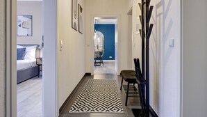 Un pasillo con un tapete estampado, una cama con almohadas, una silla y una pared azul de fondo.