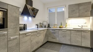 Una cocina moderna con gabinetes grises, un microondas empotrado y un ventanal con persianas.