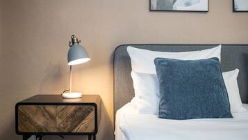 Un letto ben rifatto con cuscini bianchi e azzurri, un comodino con una lampada e un quadro appeso al muro.