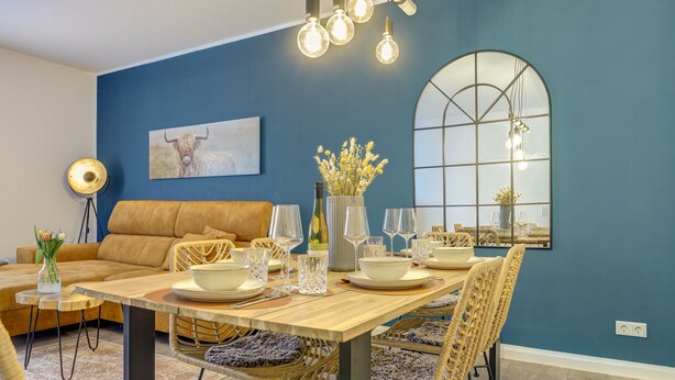 Comedor con una mesa de madera dispuesta para cuatro personas, rodeado de sillas de mimbre con asientos acolchados.