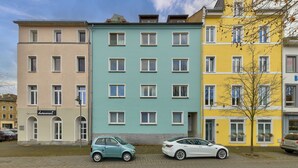 Una hilera de edificios residenciales de varios pisos, con fachada plana, coches estacionados y cielo despejado.