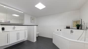 A modern bathroom with a white vanity, a bathtub, and a toilet.