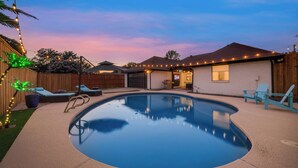 A backyard with a swimming pool, lounge chairs, and string lights. - Ultimate Comfort & Modern Elegance in our Renovated Pool House with Hot Tub (Carrollton)