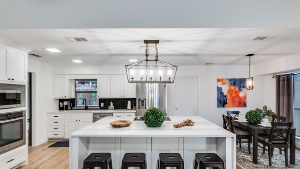 A modern kitchen with white cabinetry, a central island with stools, a stainless steel refrigerator, and a pendant light above the island. - Ultimate Comfort & Modern Elegance in our Renovated Pool House with Hot Tub (Carrollton)