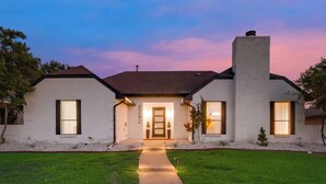 A two-story house with a central entrance, a chimney, and a well-maintained lawn. - Ultimate Comfort & Modern Elegance in our Renovated Pool House with Hot Tub (Carrollton)