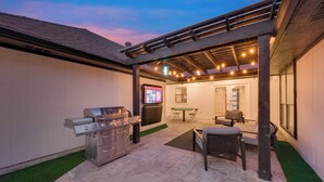 An outdoor patio area with a grill, seating, and a pergola with string lights. - Ultimate Comfort & Modern Elegance in our Renovated Pool House with Hot Tub (Carrollton)
