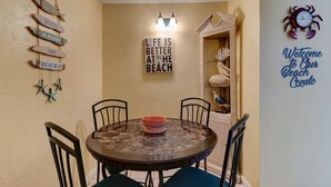 A dining area with a round table, chairs, and a wall with decorative signs and a welcome sign. - Sunrise Seven Deluxe Oceanfront Condo (Daytona Beach)