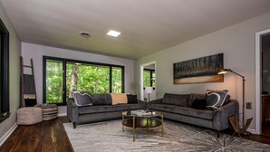 A modern living room with two sofas, a coffee table, and a large window with a view of trees.