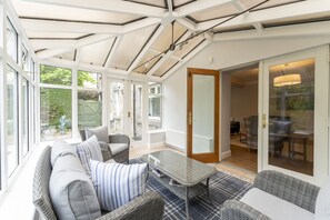 Ein sonnendurchfluteter Raum mit Glastür zu einer Terrasse, möbliert mit einer Couch, Sesseln und einem Tisch.