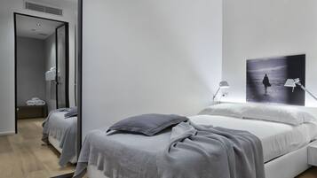 A modern bedroom with a large bed, a bedside table, a mirror, and a wall-mounted picture.
