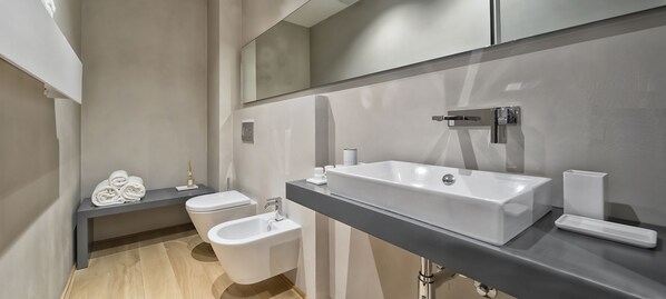 Une salle de bain moderne avec un grand lavabo, un bidet, des toilettes et un banc avec des serviettes.