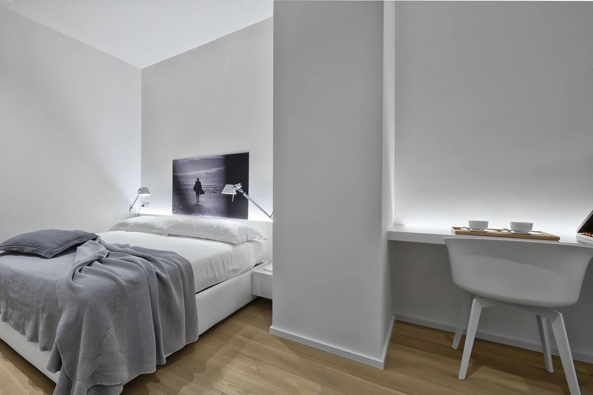 A modern bedroom with a bed, bedside table, and a desk with a chair.