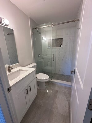 A bathroom with a glass-enclosed shower, a white sink, and a toilet.