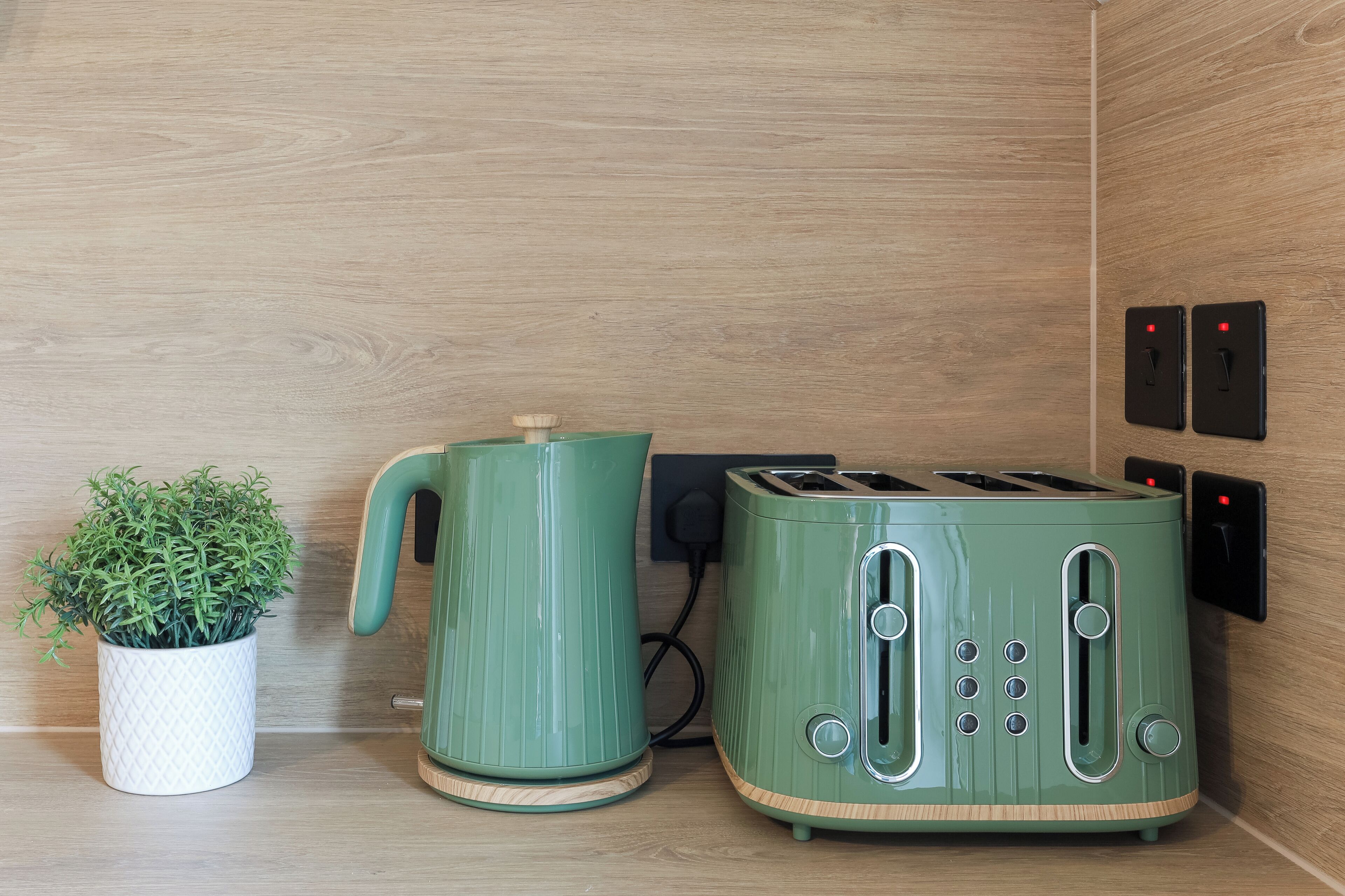 A kitchen with a green toaster, a kettle, and a potted plant.