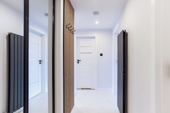 Un pasillo con una puerta blanca al final, un revestimiento de listones de madera y un radiador negro a la izquierda.