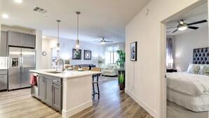 A modern kitchen with a central island, stainless steel appliances, pendant lighting, and a dining area with a sofa and table. - KingBeds Walk Score 81 Close to TPC 3021 (Scottsdale)
