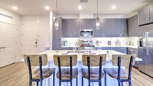 A modern kitchen with grey cabinets, stainless steel appliances, and a central island with bar stools. - KingBeds Walk Score 81 Close to TPC 3021 (Scottsdale)