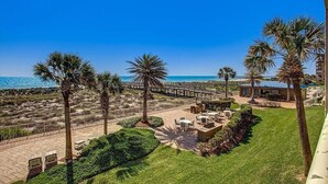 Um hotel na praia com área de pátio, palmeiras e um cais.