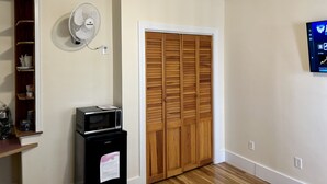 A kitchen with a microwave, a small refrigerator, a wooden door closet, a wall-mounted fan, and a TV on the wall. - Traveler’s Den in Medford (Medford)