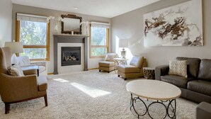 A spacious living room with a fireplace, comfortable seating, and large windows.