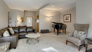 A living room with a sectional sofa, a round coffee table, a piano, and a grey armchair.