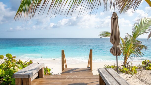 Een houten terras dat naar een strand leidt, met een bankje en een parasol.