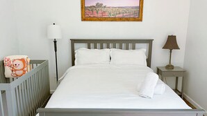 A neatly made bed with white linens, a bedside lamp, a framed picture on the wall, and a teddy bear on the side table. - Charming Vacaville Home in Peaceful Neighborhood! (Vacaville)