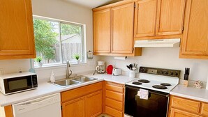 A compact kitchen with wooden cabinets, a microwave, a dishwasher, a stove, and a sink. - Charming Vacaville Home in Peaceful Neighborhood! (Vacaville)