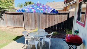 A patio with a round table and four chairs, a colorful umbrella, a wooden fence, and a barbecue grill. - Charming Vacaville Home in Peaceful Neighborhood! (Vacaville)
