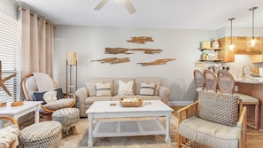 A living room with a sofa, chairs, a coffee table, and a kitchen area with wooden cabinets and a sink.