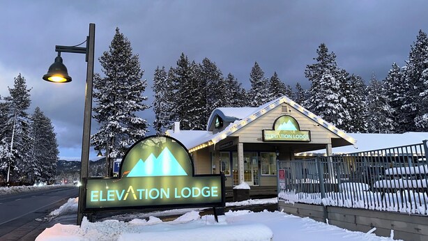 Schild für Elevation Lodge mit Berglogo, umgeben von schneebedeckten Bäumen.