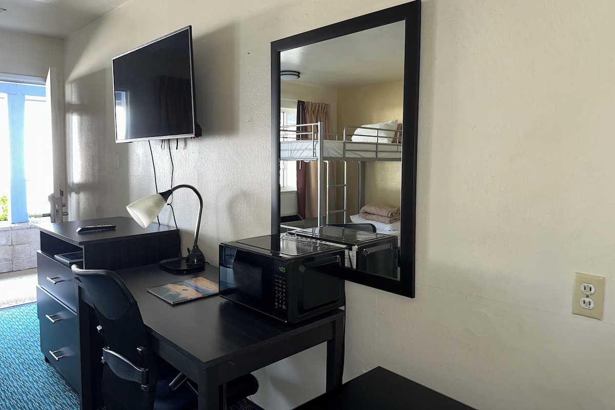 A hotel room with a desk, a TV, a mirror, a bunk bed, and a microwave.