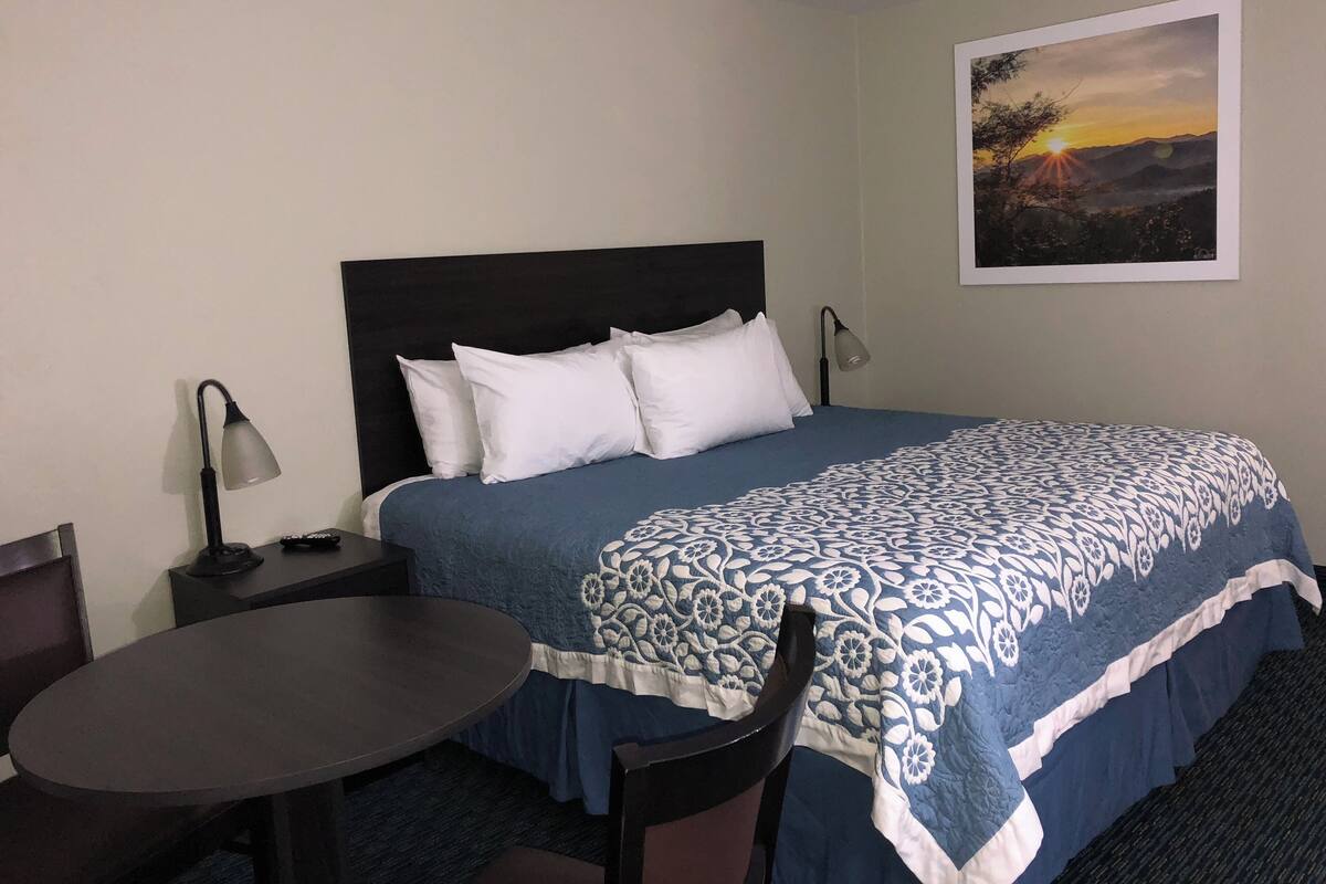 A hotel room with a bed, a desk, a chair, a lamp, and a painting on the wall.