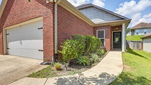 A residential house with a brick exterior, a white garage door, and a front yard with a small tree and a pathway leading to the door. - Birmingham Home w/ Yard - 15 Mi to Downtown! (Birmingham)