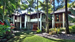 Un immeuble à plusieurs étages doté d’une cour intérieure bordée de palmiers et de plantes tropicales.