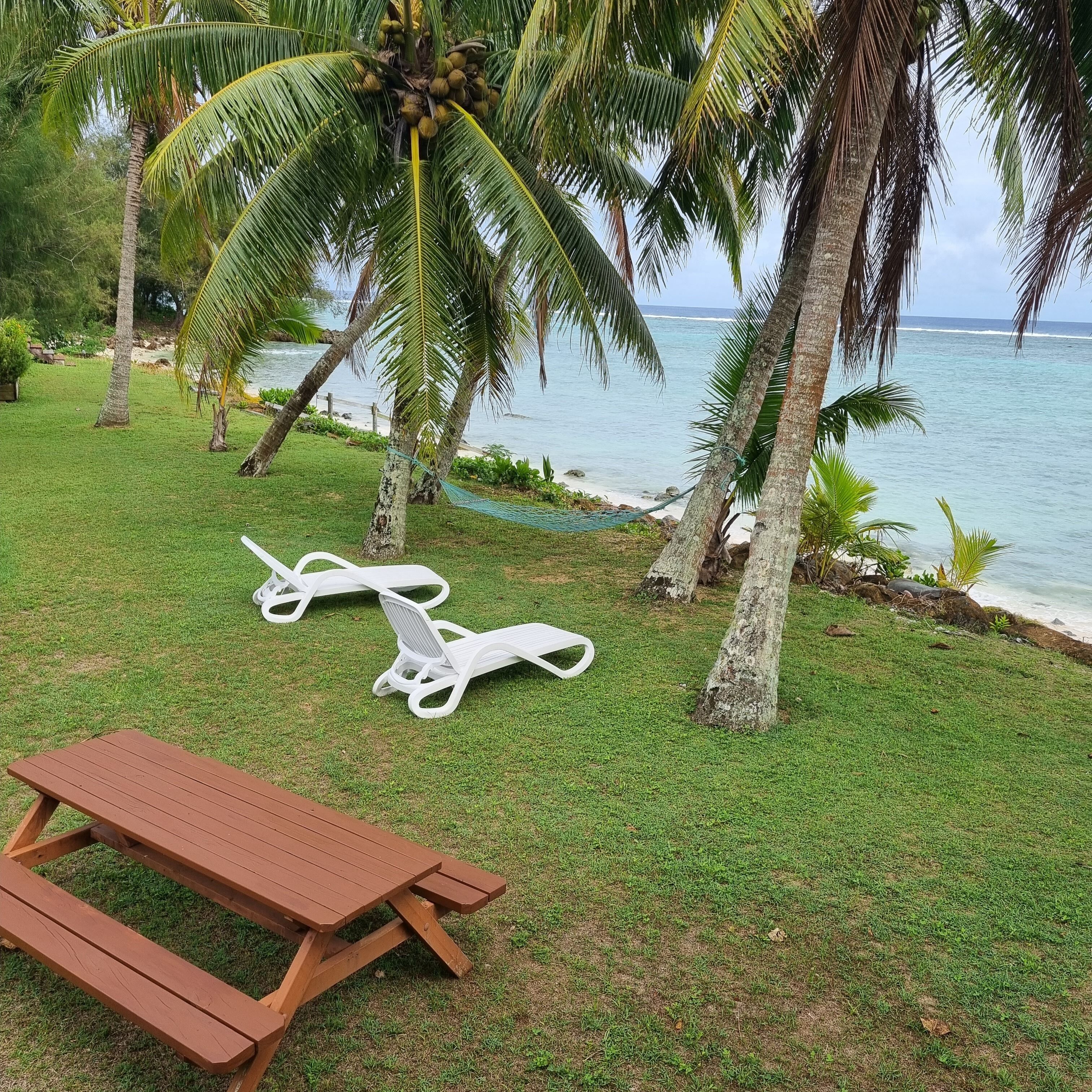 A grassy area with a wooden picnic table and two white lounge chairs.