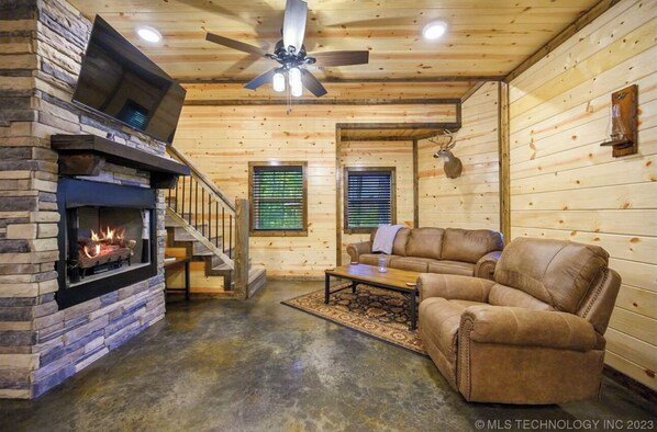 A log cabin interior with a stone fireplace, leather sofa, and a ceiling fan. - The "Bear with Me" Cabin is Perfect! (Broken Bow)