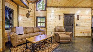 A log cabin interior with a leather sofa, a leather armchair, a wooden coffee table, and a patterned rug.