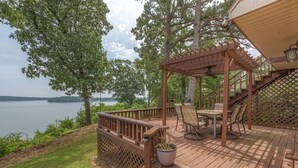 Eine Holzterrasse mit einer Pergola, Sitzgelegenheiten im Freien und Blick auf einen See.