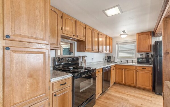 Kitchen area with oven, stove, and refrigerator, featuring a small countertop and window with blinds.