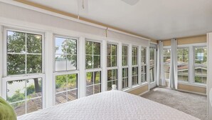 Ein Schlafzimmer mit großen Fenstern, einem Bett und einem Deckenventilator.