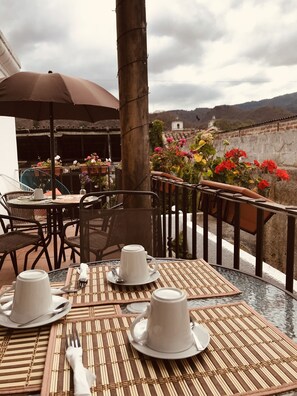 Une terrasse avec des tables dressées pour le repas, offrant une vue sur un paysage montagneux.